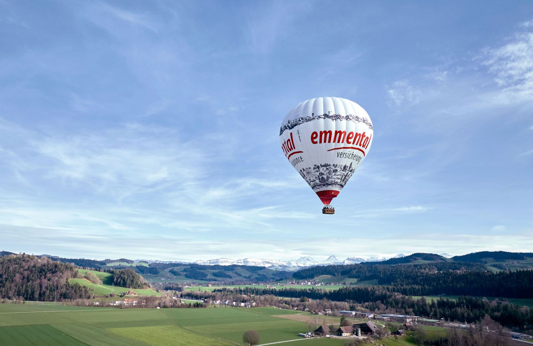 Ein Heissluftballon im Design der emmental versicherung fliegt über die Landschaft des Emmentals.