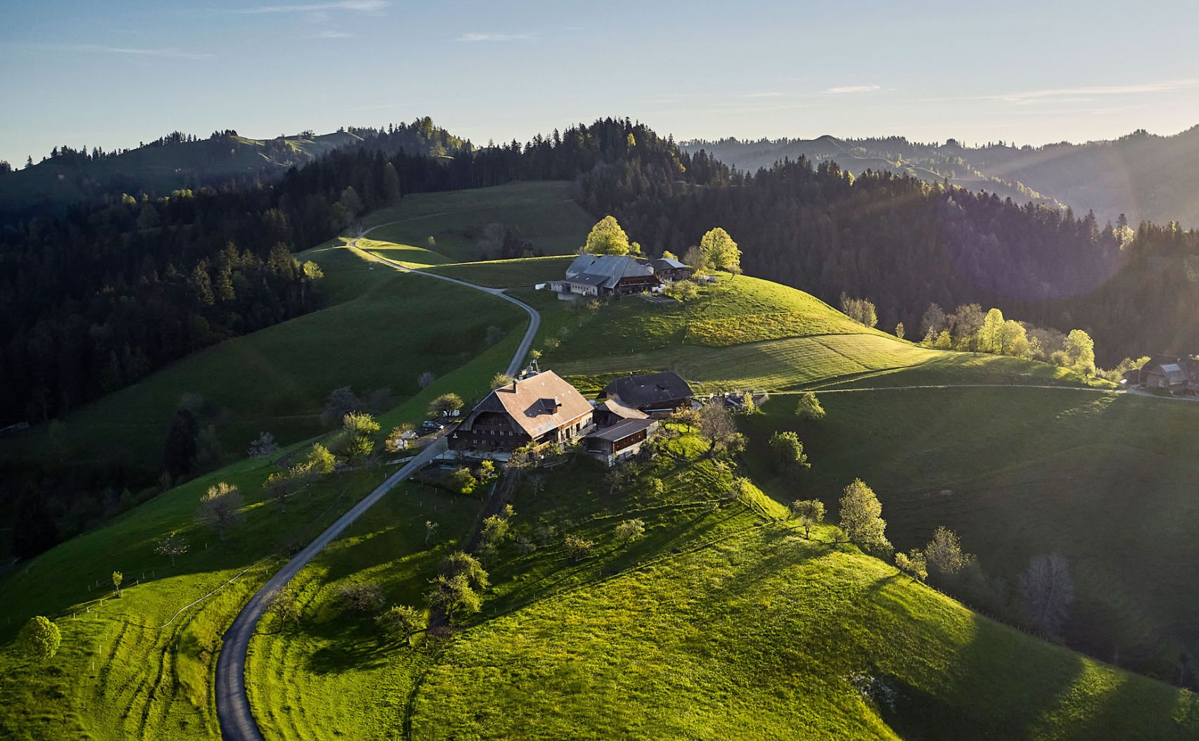 Eine hüglige Landschaft im Emmental während eines sonnigen Tages im Frühling mit grünen Wiesen und Wäldern.