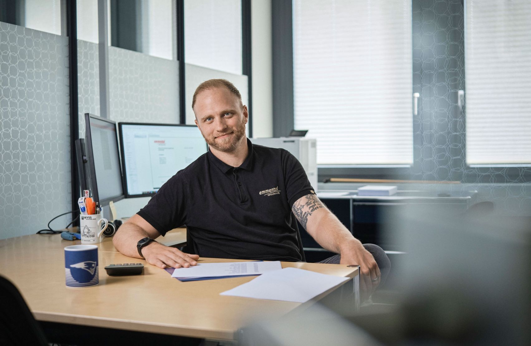 Ein Mitarbeiter der emmental versicherung sitz an seinem Arbeitsplatz und blickt freundlich in die Kamera.