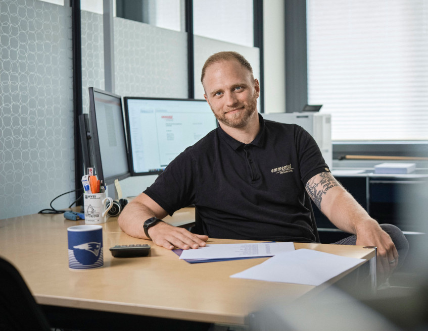 Ein Mitarbeiter der emmental versicherung sitz an seinem Arbeitsplatz und blickt freundlich in die Kamera.