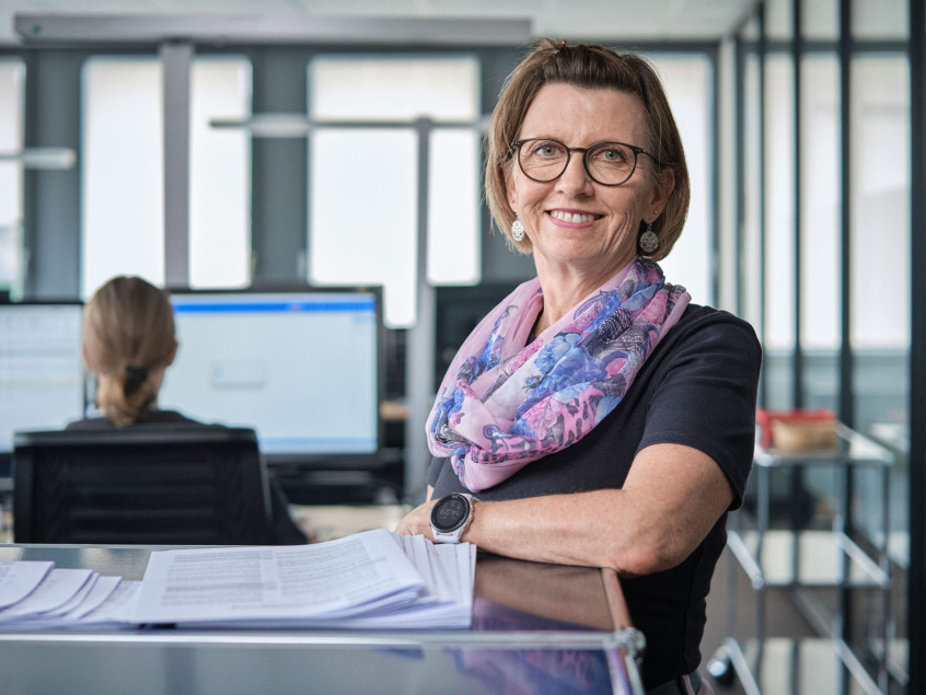 Eine Mitarbeiterin der emmental versicherung steht vor einem hüfthohen Bücherregal und lächelt freundlich in die Kamera.
