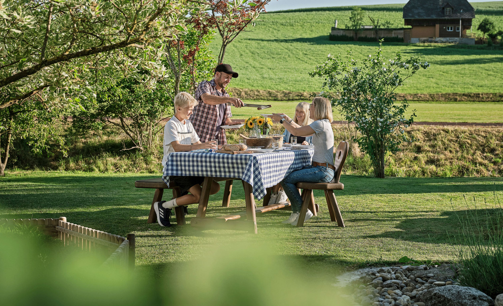 Eine Familie sitzt an einem Sommertag an ihrem Esstisch im Garten und isst gemeinsam ihr Abendbrot.