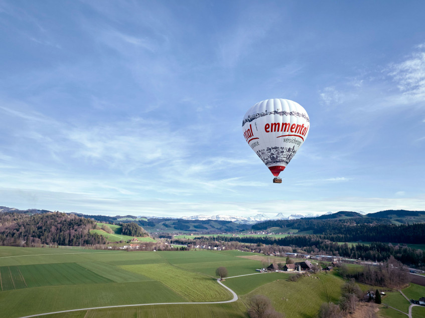 Ein Heissluftballon im Design der emmental versicherung fliegt über die Landschaft des Emmentals.