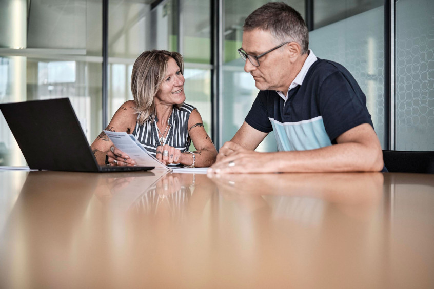 Eine Kundenberatin der emmental versicherung sitz mit einem Kunden an einem Tisch und berät diesen.