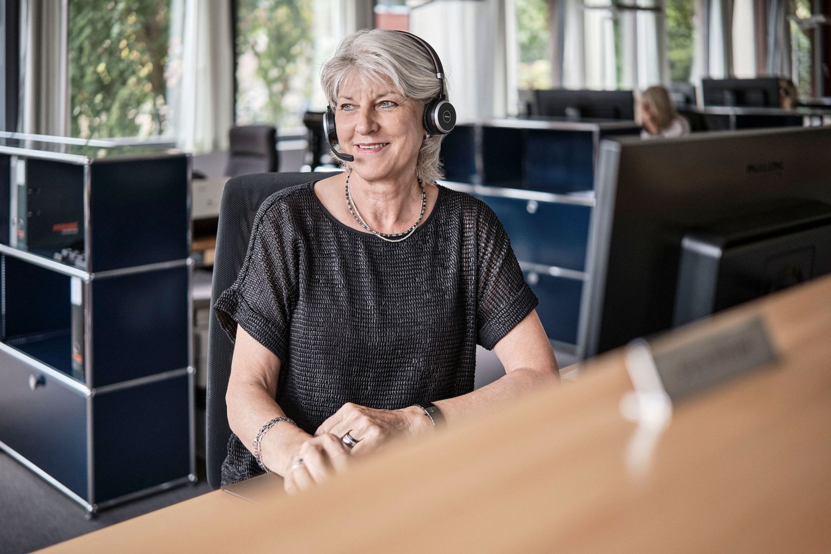 Eine Mitarbeiterin der emmental versicherung sitz an ihrem Arbeitsplatz und ist über ihr Headset am telefonieren.