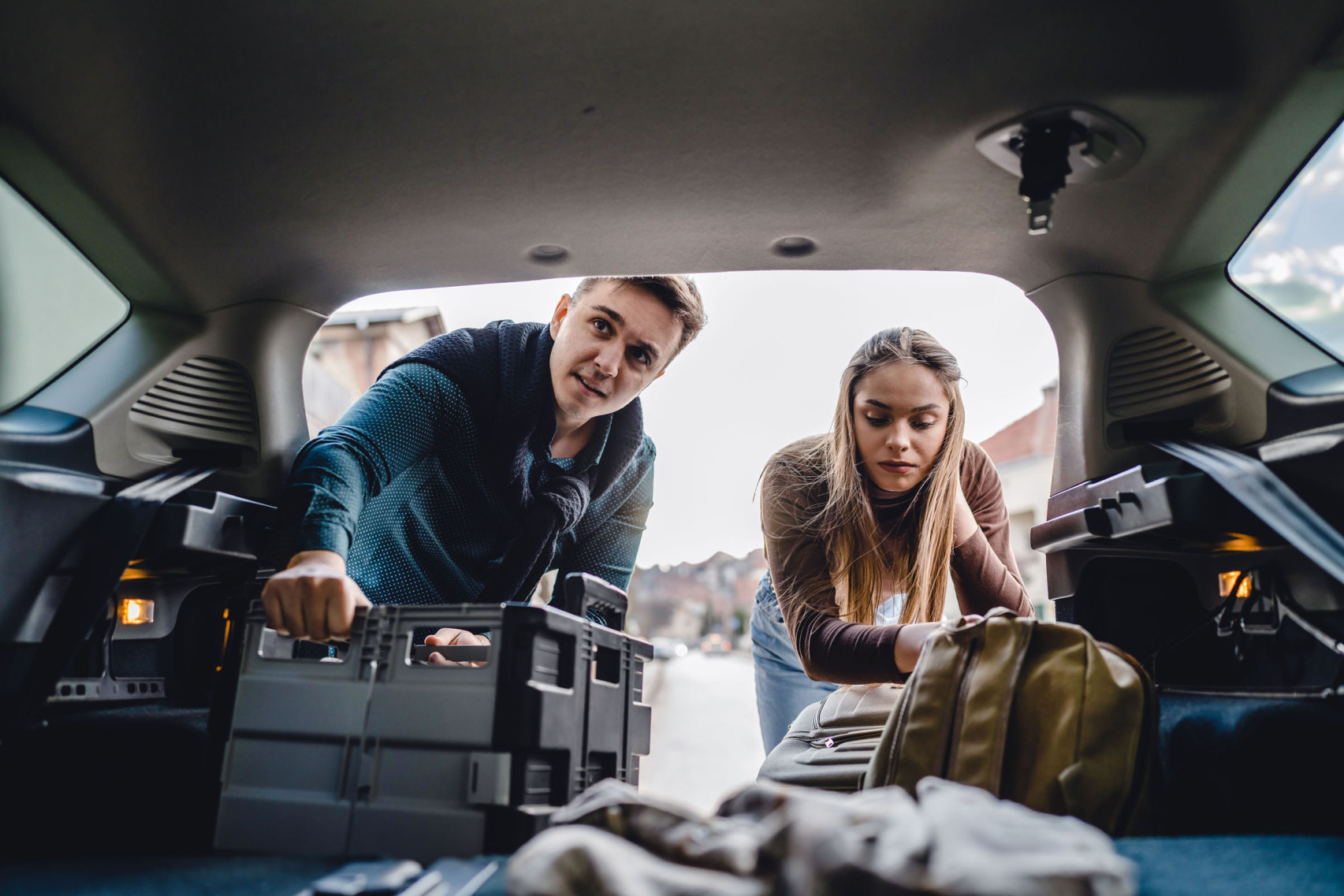 Ein junges Paar belädt den Kofferraum eines Autos.